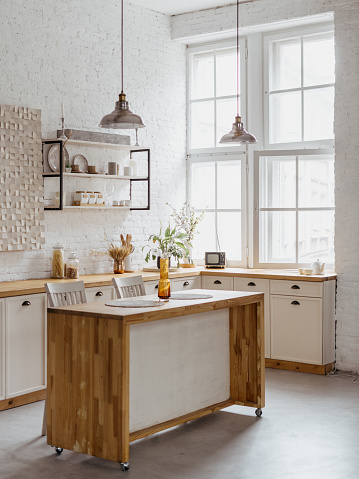 Interior design of kitchen, nobody at home. Wooden furniture, dining table with minimalistic decor at modern rural house. Vertical shot of room with white brick wall, shelves, tabletop for cooking.