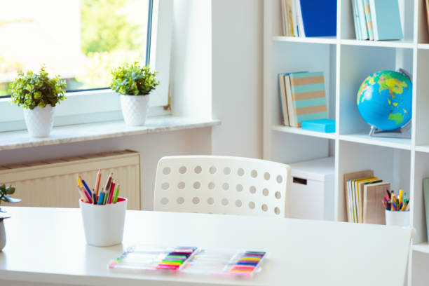 Interior of child room with white table and colorful pencils on him and shelf with books stock photo