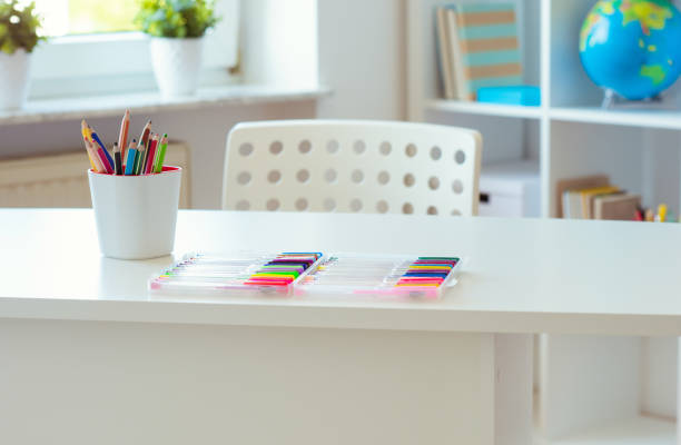 Interior of child room with white table and colorful pencils on him and shelf with books stock photo