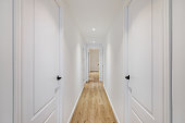 istock Interior of long narrow hallway with closed doors, wooden floor and white walls in apartment designed in minimal style 1324230669