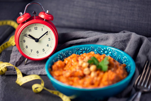 Intermittent Fasting – Weight Loss Losing weight with intermittent fasting gets more and more popular, here showed with a clock and traditional, vegan Chana Alu Masala, an indian dish intermittent fasting stock pictures, royalty-free photos & images