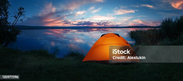 istock Internally lit orange tent on shore of lake under dramatic sunset sky 1359711196