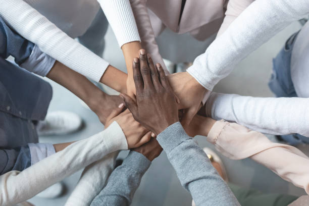 International business team putting hands together in cooperation Top view of international business team showing cooperation with putting their hands together on top of each other diversity stock pictures, royalty-free photos & images
