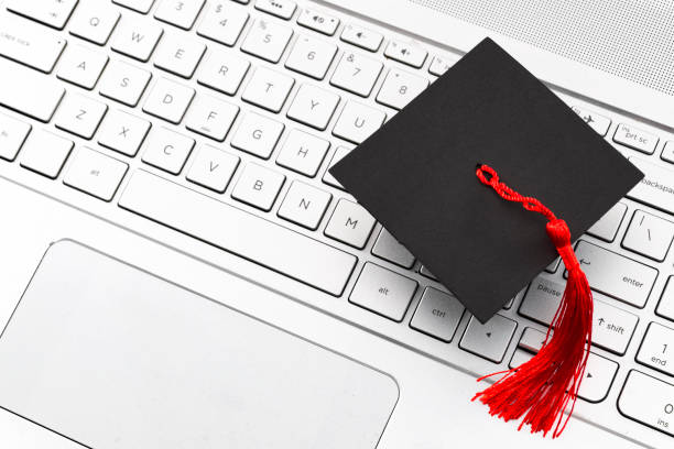 Internet academic learning, e-learning and online college education concept theme with close up on graduation cap with red tassel on computer keyboard with copyspace Internet academic learning, e-learning and online college education concept theme with close up on graduation cap with red tassel on computer keyboard with copy space degree online stock pictures, royalty-free photos & images
