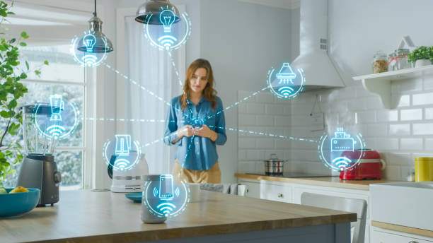 Internet of Things Concept: Young Woman Using Smartphone in Kitchen. She controls her Kitchen Appliances with IOT. Graphics Showing Digitalization Visualization of Connected Home Electronics Devices Internet of Things Concept: Young Woman Using Smartphone in Kitchen. She controls her Kitchen Appliances with IOT. Graphics Showing Digitalization Visualization of Connected Home Electronics Devices home automation stock pictures, royalty-free photos & images