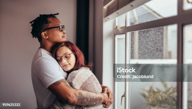 Interracial couple hugging near window