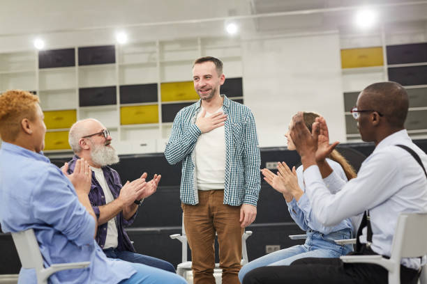Introduction at Support Group Meeting Portrait of smiling mature man    introducing himself during therapy session in support group to people clapping, copy space rehabilitation stock pictures, royalty-free photos & images