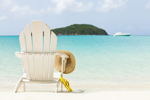 white adirondack chair, yellow flip-flops and summer hat on tropical beach in Virgin Islands