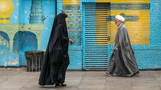Qom, Iran - May 2019: Iranian man and woman in black dress walking in a street in the sacred city of Qom