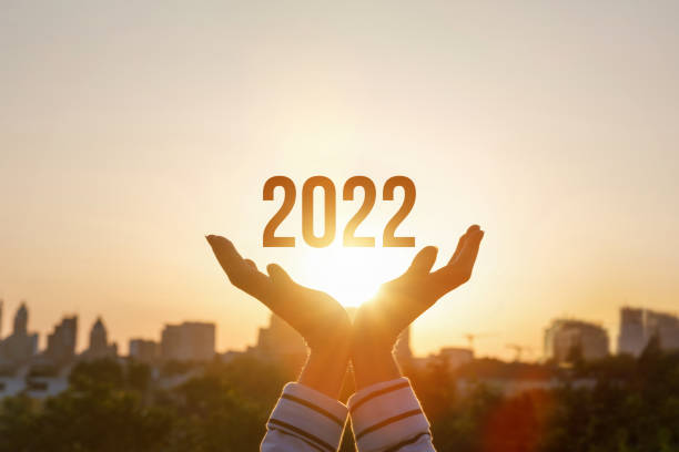2022 is supported by hands on the background of a sunny sunset. stock photo