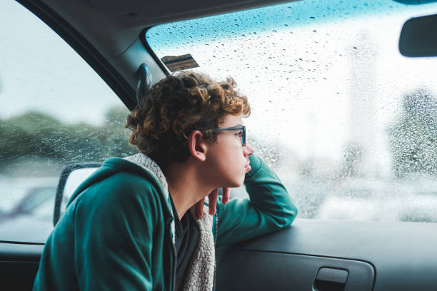 Is this rain ever going to stop? Cropped shot of a young boy sitting and looking bored while looking out the car window during a rainstorm brat stock pictures, royalty-free photos & images