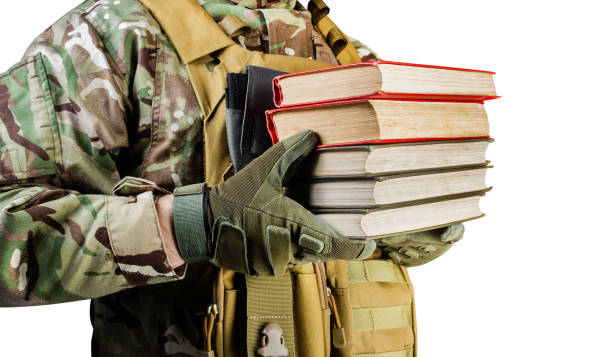Isolated photo of a soldier in uniform holding stack of books. Isolated photo of a soldier in uniform holding stack of books on white background, side view. military colleges stock pictures, royalty-free photos & images