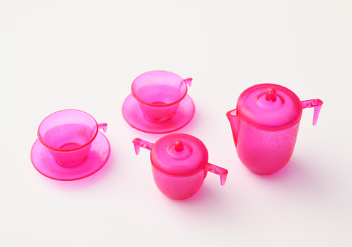 High angle view of miniature pink toy plastic tea set on white background.