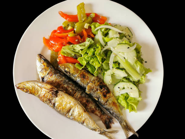 Isolated view of plated food, healthy fish meal, typical dish of Portuguese regional cuisine with grilled sardines with salad: red peppers, green peppers, sesame seeds, lettuce, onion and cucumber stock photo