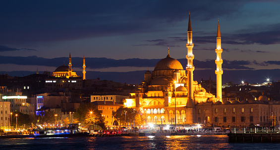 Istanbul Yeni Cami and Nuruosmaniye Mosques at night panorama with the Bosphorus River in the foreground.