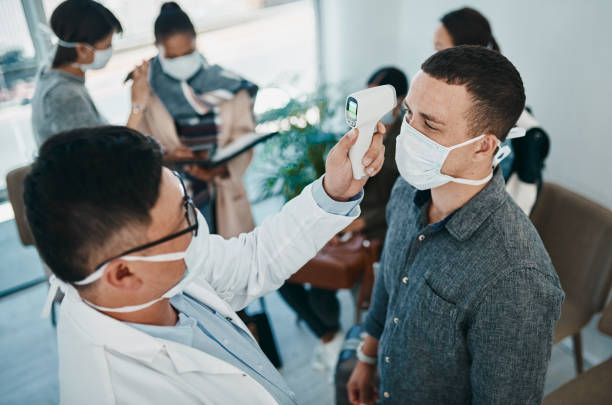 It all starts with a fever Shot of a young man getting his temperature taken with an infrared thermometer by a healthcare worker during an outbreak south africa covid stock pictures, royalty-free photos & images