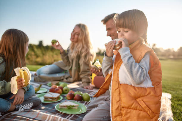 It tastes good. Happy family spending time in the park on a sunny day Portrait of little boy eating sandwich. Young parents having picnic with their children on blanket in park. Family and kids, nature concept. Horizontal shot picnic stock pictures, royalty-free photos & images