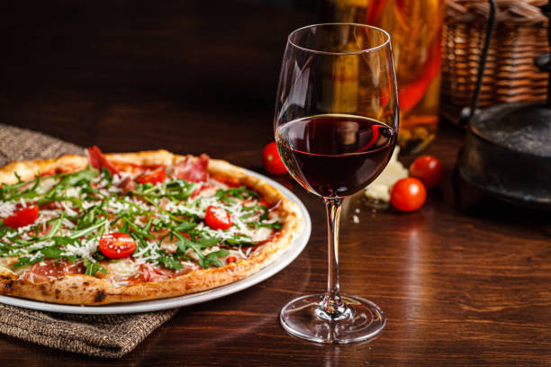 Italian food. Classic thin pizza with large sides, prosciutto, cherry tomatoes, arugula, parmesan cheese. Serving dishes in a restaurant on a white plate with red wine. stock photo
