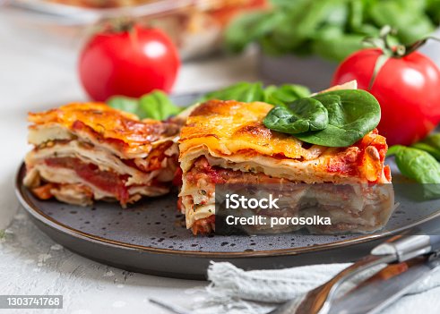 istock Italian lasagna with tomato sauce and cheese served with tomatoes and spinach, light concrete background. Homemade vegetarian lasagna. 1303741768