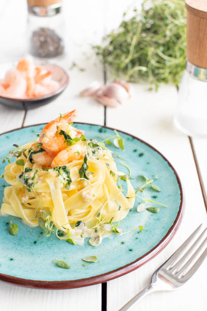 Italian pasta fettuccine in a creamy sauce with shrimp and spinach on a plate stock photo