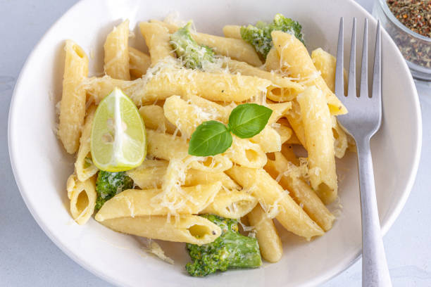 Italian Penne Pasta with Broccoli Garnished with Fresh Basil Leaves and Lemon Top Down Horizontal Photography stock photo