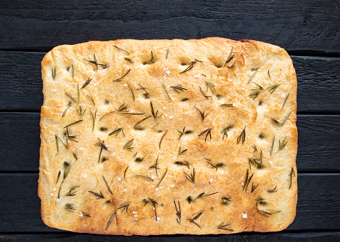Italian rustic bread - classic focaccia with rosemary and olive oil on a black wooden background - top view and copy space