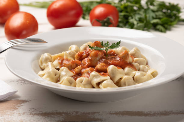 Italian tortellini (capeletti, agnolini) with tomato sauce in a white plate on rustic white wooden table background stock photo
