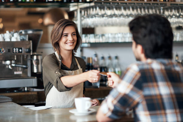 It's a pleasure to be of service Shot of a cheerful female bartender receiving a card as payment from a customer inside of a restaurant barista stock pictures, royalty-free photos & images