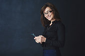 Studio portrait of a corporate businesswoman texting on a cellphone against a dark background