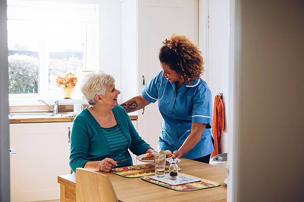 It's Dinner Time! Care worker giving an old lady her dinner in her home. home caregiver stock pictures, royalty-free photos & images