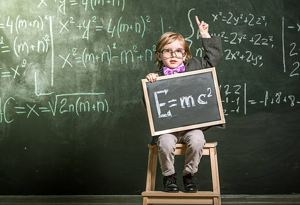 It's everyone should know Brainy little boy sitting in front of blackboard. Boy showing the mass-energy equivalence formula on small chalkboard e=mc2 stock pictures, royalty-free photos & images