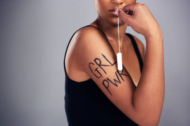 Studio shot of a young woman with “grl pwr” painted on her arm posing against a grey background