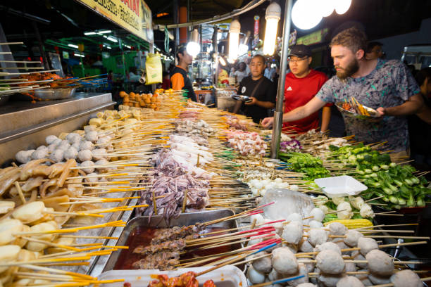 Jalan Alor Bukit Bintang Kuala Lumpur Kuala Lumpur, Malaysia - January 28, 2017: Tourist selecting food from a Lok-Lok market stall street food restaurant at the night market on Jalan Alor located in the Bukit Bintang area of Kuala Lumpur, Malaysia. Jalan Alor is a foodie heaven and is a popular eating destination for both tourists and locals. Lok-lok is a dish consisting of various deep-fried foods such as meats and vegetables that are served on a skewer. bukit bintang stock pictures, royalty-free photos & images
