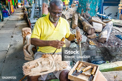 istock Jamaican man uses hand tools to carve a decorative art sculpture from raw wood 1342091725