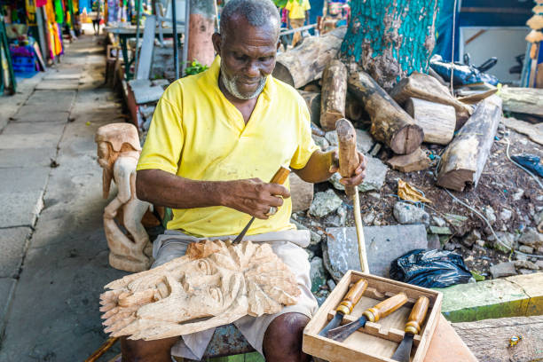 Jamaican man uses hand tools to carve a decorative art sculpture from raw wood stock photo