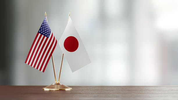 Japanese and American flag pair on desk over defocused background. Horizontal composition with copy space and selective focus.