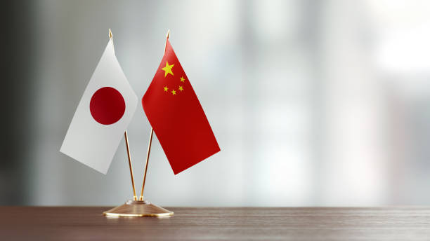 Japanese and Chinese flag pair on desk over defocused background. Horizontal composition with copy space and selective focus.