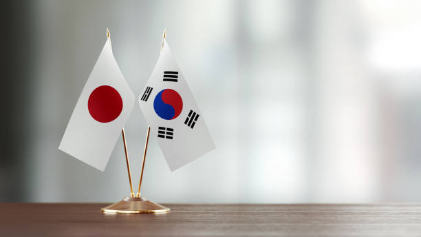 Japanese and South Korean flag pair on desk over defocused background. Horizontal composition with copy space and selective focus.