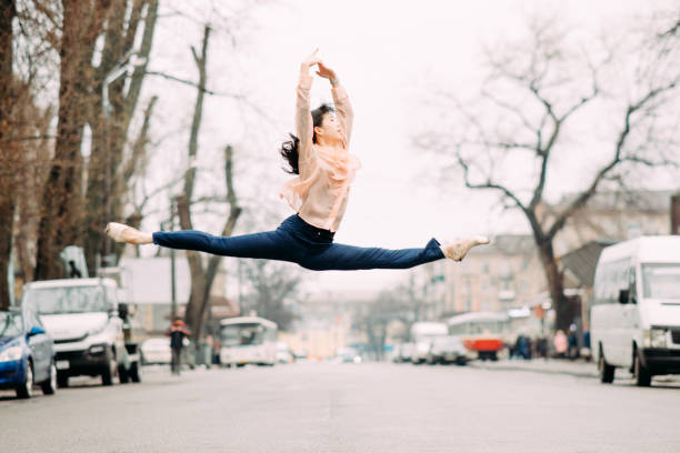 Japanese ballerina performs split and jumps in the city street. Japanese ballerina performs split and jumps in the city street against the background of cars. doing the splits stock pictures, royalty-free photos & images