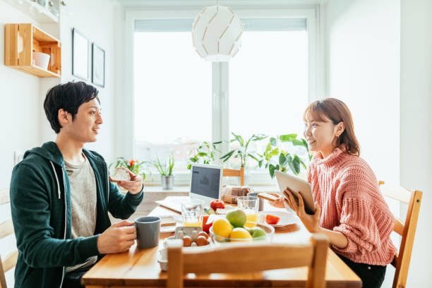 自宅で日本人カップル、キッチンで一緒に食事をし、リモートワークのための技術を使用 - 結婚生活 ストックフォトと画像