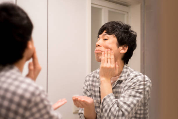 Japanese man in pajamas doing skin care in bathroom at home stock photo
