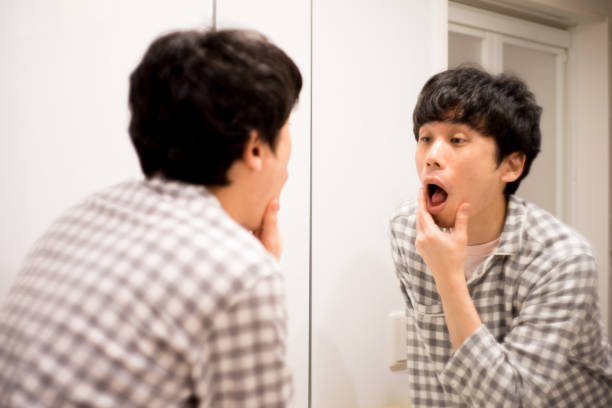 Japanese man in pajamas worries about sore throat in bathroom at home stock photo
