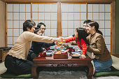 日本の部屋の食卓で、お飾ちりり、日本の新年料理を食べる前に乾杯を飲む日本のミューラ世代の家族