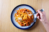 日本のパスタ料理、スパゲッティ(ナポリータン)のレシピ。皿の上のナポライトは薄い木目のテーブルの上に置かれる。フォークが絡み合った祖母のスパゲッティ。