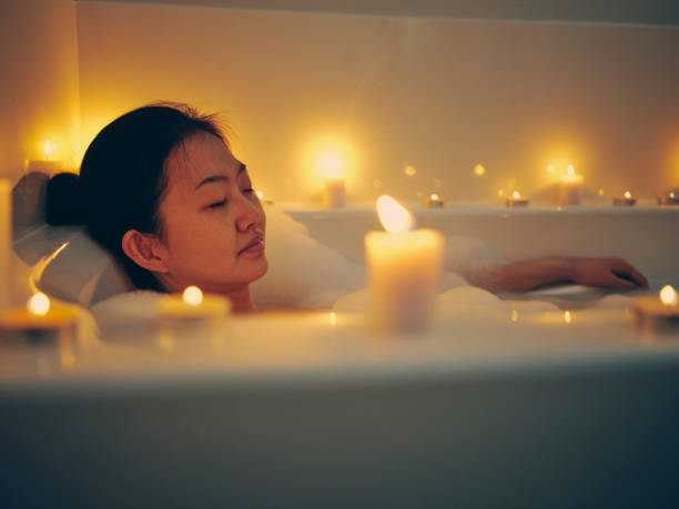 Japanese Woman Taking a Candlelight Bath A young Japanese woman relaxing in a bathtub, surrounded by candles. WARM BATH stock pictures, royalty-free photos & images