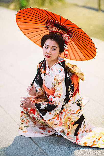 Japanese woman with oil paper umbrella Beautiful japanese woman stand on the floor outside during a lovely sunny day. She wears kimono, obi and hold oil paper umbrella.The kimono is very colorful and elegant. She seems very pensive. There is beautiful kanzashi in her hair. furisode stock pictures, royalty-free photos & images