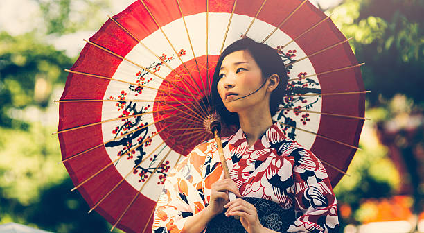 Japanese woman with oil paper umbrella Beautiful japanese woman stand in the park. She wears kimono, obi and hold oil paper umbrella.The kimono is very colorful and elegant. She seems very pensive.  furisode stock pictures, royalty-free photos & images