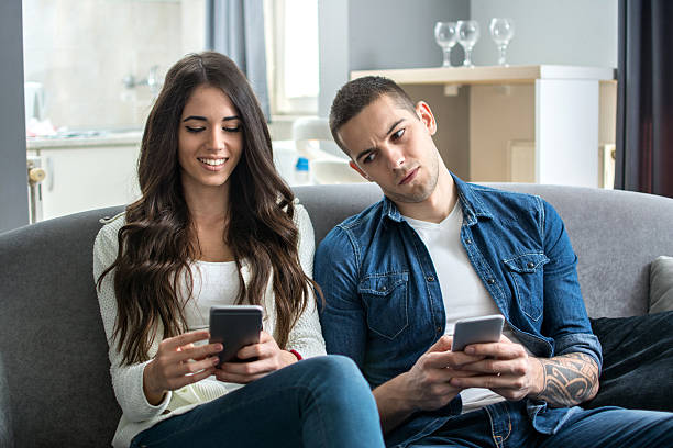 Jealous boyfriend spying his girlfriend's phone. Young couple using smartphones at home. Jealous boyfriend spying his girlfriend's phone. envy stock pictures, royalty-free photos & images