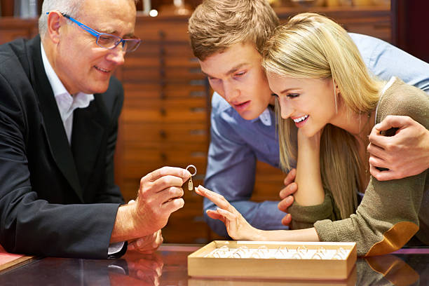 Jewelry can speak volumes about your personality Mature jewelry store clerk assisting a couple in choosing an engagement ring store clerk selling jewelry stock pictures, royalty-free photos & images
