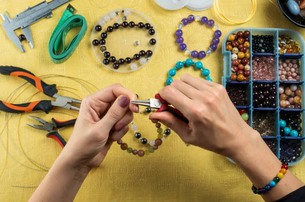 Jewelry making. Female hands with a tool on a yellow background stock photo